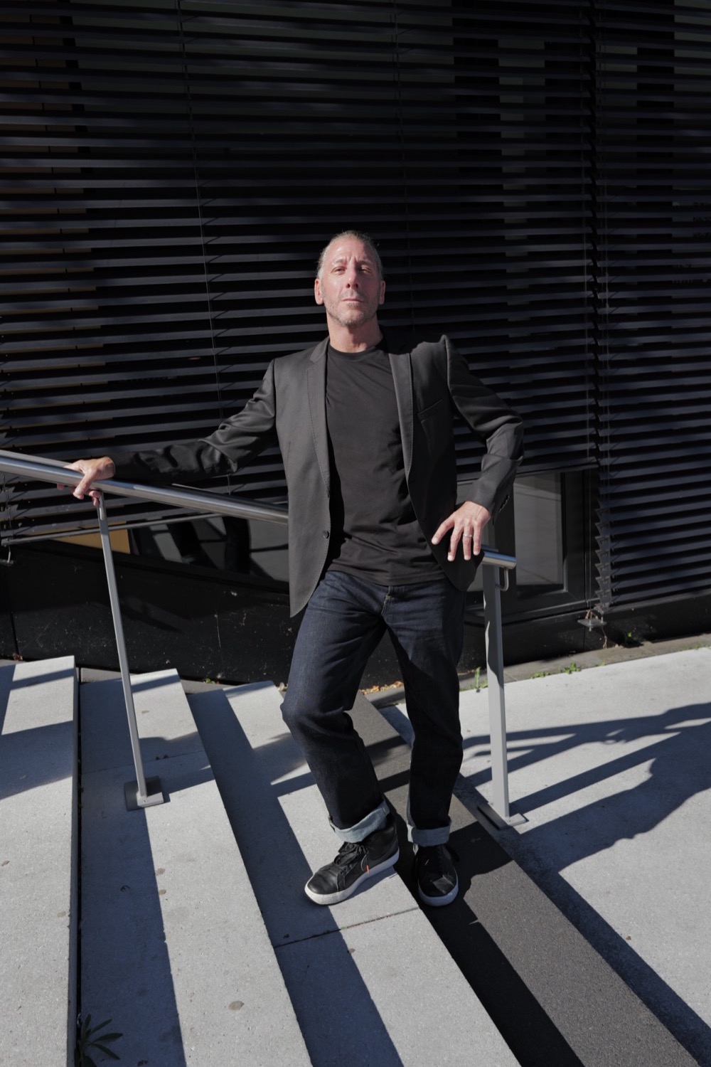 Business-Portrait outdoor in Aachen: Mann im Sakko auf einer Außentreppe vor schwarzer Lamellenfassade