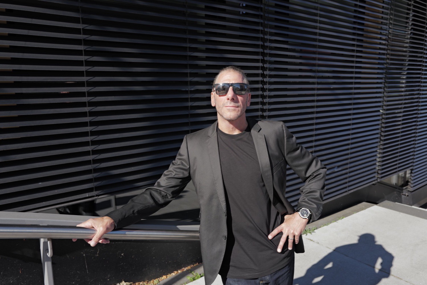 Mann mit Sonnenbrille am Treppengeländer vor schwarzer Lamellenfassade