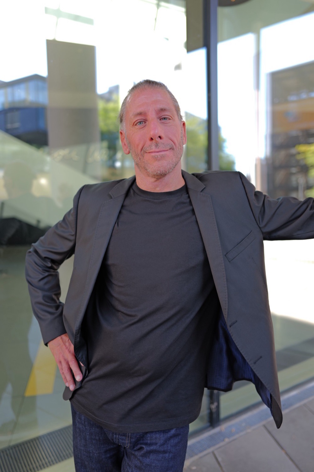 Business-Portrait vor einer großen Glasfront in Aachen, Sakko offen, lächelnd