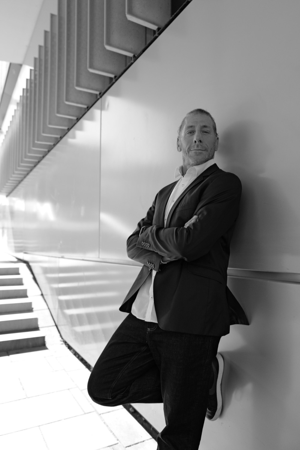 Schwarzweiß-Business-Portrait im weißen Hemd an einer hellen Wand unter einer Treppe