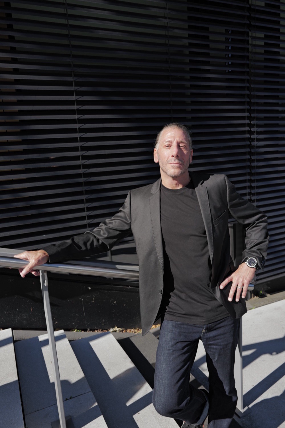 Portrait am Geländer vor einer Lamellenfassade in der Sonne