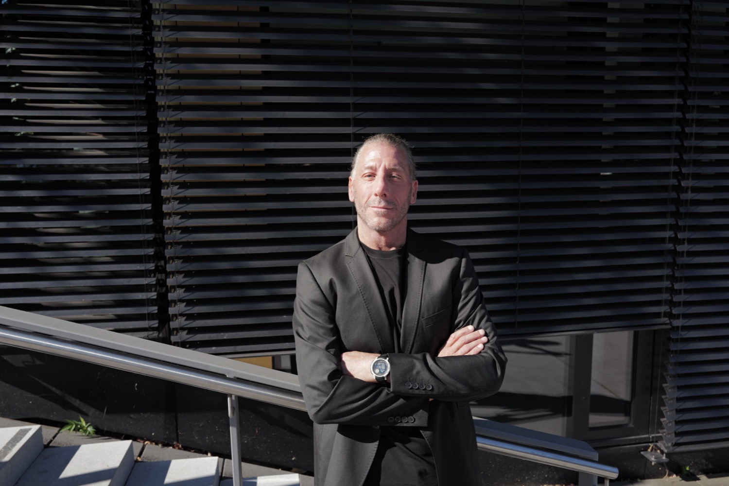 Business-Portrait mit verschränkten Armen vor schwarzer Lamellenfassade