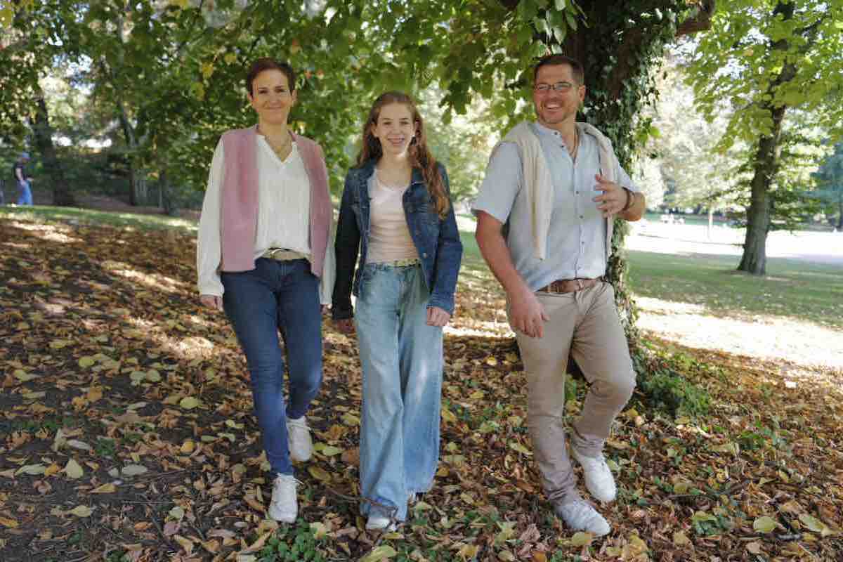 Mutter, Tochter und Vater laufen lachend durch Herbstlaub im Park