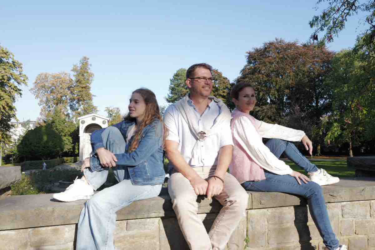 Familie sitzt Rücken an Rücken auf einer Steinmauer in der Sonne