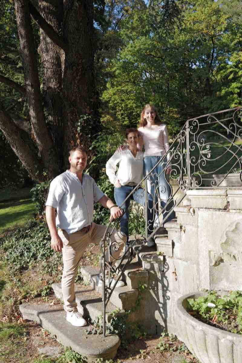 Familie auf einer alten Steintreppe mit Eisengeländer neben einem großen Baum