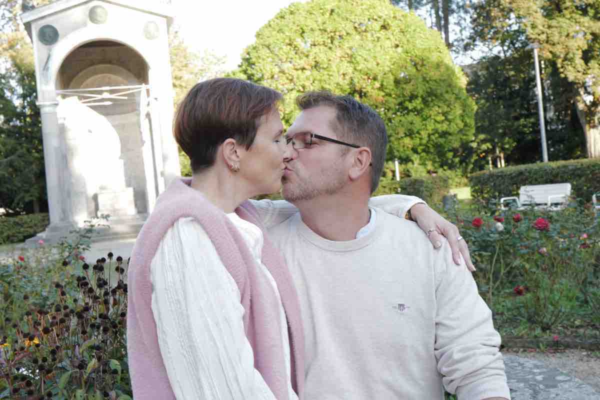 Paar küsst sich im Rosengarten vor einem weißen Denkmal